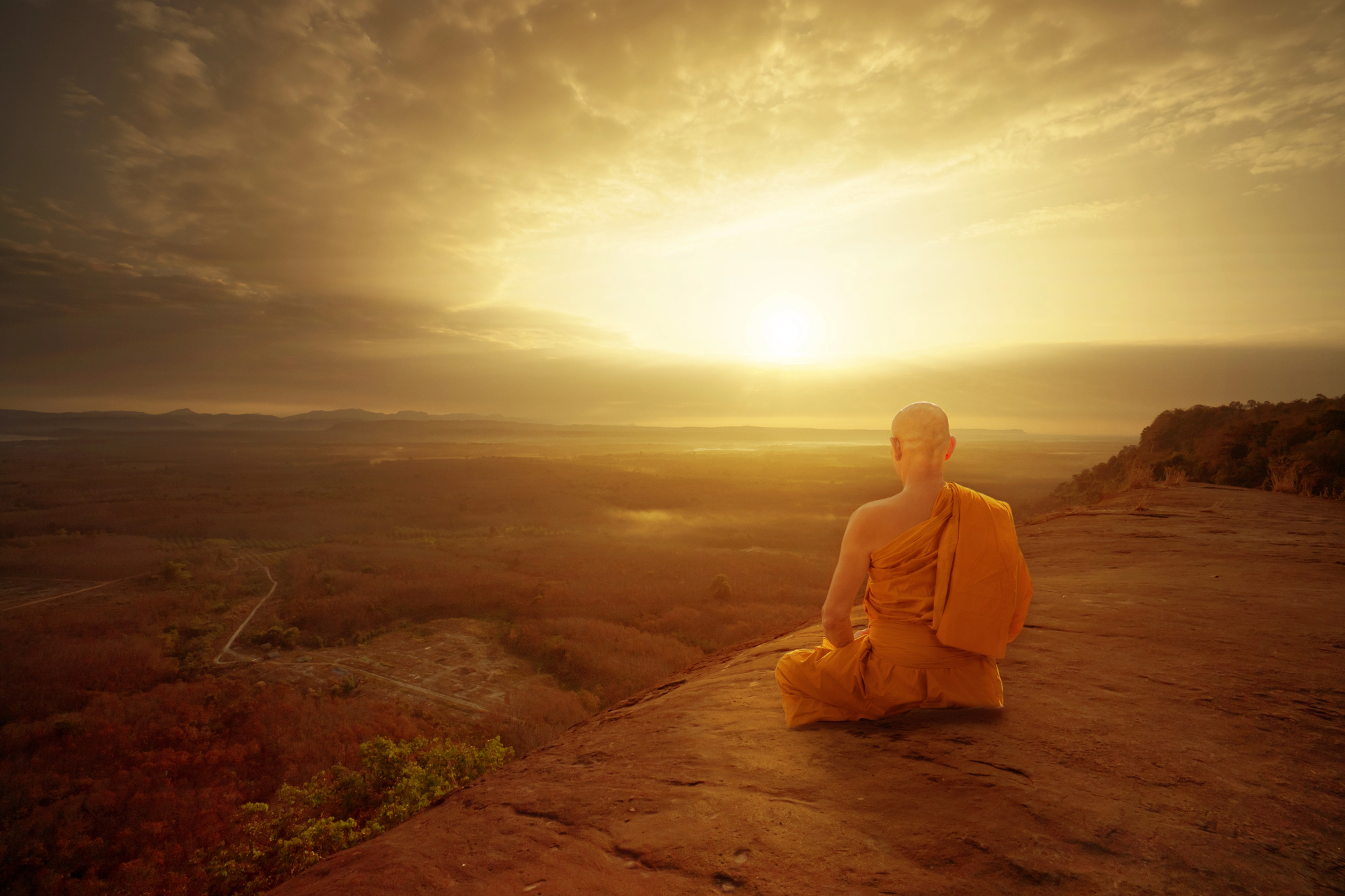 A buddhist monk meditates in the desert at sunrise.